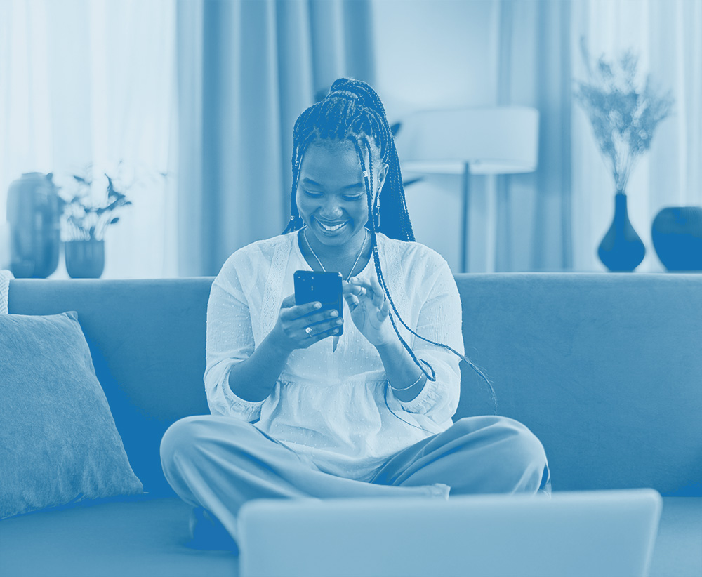 Women sat crossed legged on the sofa looking at her phone